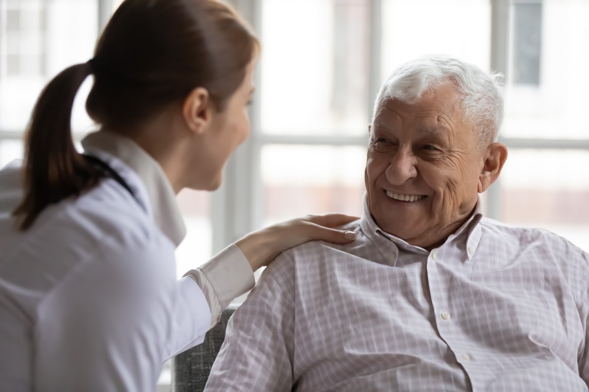 Carer In White Coat Cares For Elderly Man