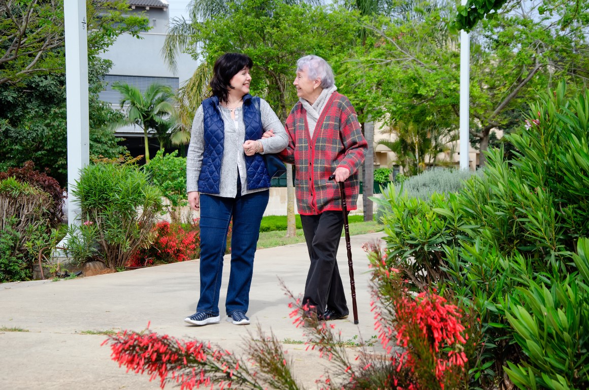 Female Caregiver And Senior Adult Woman Are Walking arm in arm